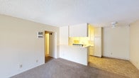 Located at 501-567 Canyon in Oceanside, this single-story unit offers a practical and well-organized layout throughout. The living area is generously proportioned, featuring neutral carpet flooring and a textured ceiling. A sliding glass door fitted with vertical blinds allows natural light to filter in while providing outdoor access. The open-concept design connects the living space to the kitchen via a peninsula-style half-wall, creating a functional pass-through arrangement.

The kitchen is designed as a galley-style space with ample white cabinetry extending from counter height to ceiling, providing substantial storage. It includes a stainless steel double sink, a dishwasher, a refrigerator, and tile flooring that contrasts with the carpeted living areas. Under-cabinet lighting adds warmth to the workspace.

The bedrooms are carpeted and bright, each featuring large windows with vertical blinds that bring in natural light and outdoor views of surrounding greenery. One bedroom offers dual closets, maximizing storage capacity.

The bathroom is clean and functional, featuring tile flooring, a combined tub and shower with a curtain rod, a toilet, and a vanity with an integrated sink. Neutral tones throughout the unit create a cohesive, understated aesthetic well-suited for comfortable everyday living.
