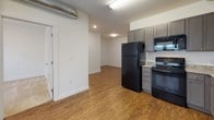 This two-bedroom, two-bathroom unit is thoughtfully laid out across a single floor, maximizing functionality within a compact footprint. The open living and kitchen area serves as the heart of the unit, featuring durable wood-style flooring that extends through the main living spaces. An exposed ductwork detail in the kitchen lends an industrial character to the space.

The kitchen is well-equipped with gray shaker-style cabinetry, granite countertops, and a full suite of black appliances, including a refrigerator, electric range, microwave, and dishwasher. Ample cabinet storage and counter space make the kitchen practical for everyday use.

Both bedrooms are carpeted and receive natural light through windows fitted with blinds. Each room offers closet access, with one bedroom featuring double doors for additional storage capacity. A thermostat panel is conveniently located in the hallway.

The two bathrooms include granite vanity countertops with undermount sinks. One bathroom features tile flooring and a window for natural ventilation, while the other includes a shower/tub combination. Clean white walls and recessed lighting throughout contribute to a bright, neutral aesthetic suited for a variety of furnishing styles.