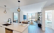 Located in Miami's vibrant Wynwood neighborhood, this contemporary residence offers a thoughtfully designed open-concept layout filled with natural light. The combined living and dining area serves as the heart of the home, anchored by expansive floor-to-ceiling windows that frame sweeping city skyline views. Light hardwood flooring runs throughout, complementing the clean, neutral palette.

The modern kitchen is a standout feature, showcasing a generous quartz waterfall island with seating for multiple guests, white flat-front cabinetry, stainless steel appliances, a subway tile backsplash, and stylish globe pendant lighting — equally suited for everyday cooking and entertaining.

The bedroom is generously proportioned, offering large windows with continued city views, creating a bright and serene retreat. Two well-appointed bathrooms feature clean, contemporary finishes, including floating wood-toned vanities, illuminated mirrors, and frameless glass-enclosed showers with crisp white tile and matte black fixtures.

Additional conveniences include a dedicated laundry area, closet, and utility room. The unit also benefits from in-unit storage solutions. Throughout the residence, a cohesive modern aesthetic is maintained with warm lighting, light wood floors, and a calm, neutral color scheme that highlights the urban Miami backdrop just outside the windows.