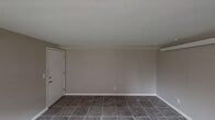 This single-floor unit offers a straightforward and functional layout designed for practical, everyday living. The main living area is generously proportioned, featuring neutral taupe walls, crisp white baseboards, and durable large-format tile flooring that extends throughout the space. A wall-mounted heating unit ensures year-round comfort, while a window along one wall allows natural light to filter in, offering views of the surrounding exterior. The open feel of this room provides flexibility for a variety of furniture arrangements.

The kitchen is well-equipped and efficient, featuring warm-toned wood cabinetry on both upper and lower levels, dark countertops, and a stainless steel sink positioned beneath a window. Essential appliances — including a refrigerator, electric range with overhead ventilation, and ample storage — make this a fully functional cooking space. Overhead flush lighting illuminates the room evenly. A doorway connects the kitchen directly to the adjacent bathroom.

The bathroom includes a full-sized bathtub with an overhead shower, a toilet, and the same tile flooring found throughout the unit, maintaining a cohesive aesthetic. The layout is compact and utilitarian. Overall, this space presents a clean, no-frills interior that is move-in ready and easy to maintain.