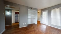 This single-floor residence offers a cohesive and functional layout designed for comfortable everyday living. Throughout the space, rich hardwood-style flooring in warm tones creates a unified aesthetic that ties each room together seamlessly.

The living area serves as the heart of the home, featuring built-in white shelving recessed into the wall — a practical and attractive storage solution. Natural light filters in through a windowed front door and a large vertical blind-covered window, brightening the open space. The textured ceiling adds a classic touch consistent throughout the unit.

The galley-style kitchen is well-equipped and visually striking, with rich dark wood cabinetry, granite-style countertops, a mosaic tile backsplash, stainless steel appliances including a refrigerator and electric range, and ample upper and lower cabinet storage on both sides of the corridor.

The bedrooms are generously proportioned, each finished with the same warm hardwood-style flooring and neutral gray walls. Windows in each room invite natural light and provide a sense of openness.

The bathroom features a dark wood vanity with granite countertops, a framed mirror, and a separate tiled shower area, combining practicality with a refined finish. Overall, the space presents a clean, modern, and move-in-ready interior.