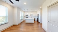 Located at 1201 Hillside Avenue in Nashville, TN, this thoughtfully designed one-bedroom, one-bathroom residence offers a clean, modern aesthetic across a single floor. The open-concept living, dining, and kitchen area serves as the heart of the home, bathed in natural light from multiple large windows with views of the surrounding neighborhood. The kitchen is a standout feature, showcasing crisp white shaker cabinetry, a classic subway tile backsplash, quartz countertops, a central island with contrasting dark-toned base cabinetry, and a full suite of stainless steel appliances including a gas range, built-in microwave, dishwasher, and French door refrigerator. Brass-accented pendant lights add a warm, contemporary touch overhead. Warm-toned hardwood-style flooring flows seamlessly throughout the entire unit, lending continuity and a welcoming feel. The bedroom is a comfortable retreat with a ceiling fan, generous natural light, and outdoor views. A den provides flexible bonus space. The bathroom is well-appointed with a tiled tub-shower combination, matte black fixtures, a white vanity, and a large mirror. Additional conveniences include in-unit laundry, a hallway, and two closets.