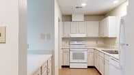 This single-story home offers a practical and functional layout, accommodating six bedrooms and two full bathrooms within a well-organized floor plan. The combined kitchen and living room serves as the heart of the home, with the living area showcasing warm wood-look hardwood flooring, a textured ceiling, and a ceiling fan with lighting. A sliding glass door with vertical blinds allows natural light to flow in. The adjacent kitchen is outfitted with white cabinetry, ample counter space, tile flooring, and a full suite of white appliances including a freestanding electric range with overhead ventilation, a dishwasher, and a refrigerator. A double-basin stainless steel sink sits beneath a window, adding natural light to the workspace. Each of the six bedrooms features the same warm wood-look flooring, textured ceilings, and ceiling fans, offering comfortable and consistent living spaces. A central hallway connects the bedrooms and bathrooms efficiently. The two bathrooms are finished with tile flooring and include a tub-shower combination. A dedicated laundry room provides in-unit washer and dryer hookups with overhead shelving for additional storage, completing this well-appointed home.