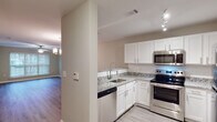 Located at 405 Thomas Burke Dr in Hillsborough, NC, this single-floor residence offers a well-designed layout with modern finishes throughout. The kitchen is a standout feature, equipped with white shaker-style cabinetry, granite countertops with a classic white-and-gray pattern, a white subway tile backsplash, and a full suite of stainless steel appliances including a range, microwave, dishwasher, and refrigerator. Track lighting illuminates the workspace, and light wood-look flooring extends throughout the main living areas. The adjacent dining area is highlighted by an elegant multi-globe chandelier and opens directly into the living room, which features a ceiling fan with light kit and a neutral color palette that enhances the sense of openness. A window in the living area allows for natural light. The bedroom is finished with plush carpeting, a ceiling fan, and a window with blinds that provides natural light. The bathroom includes a tub/shower combination with a chrome fixture, a toilet, and matching wood-look flooring that ties seamlessly into the rest of the unit. The overall ambiance is clean, modern, and move-in ready, with consistent neutral tones and quality finishes that create a comfortable, functional living environment.