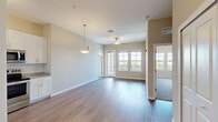 This single-floor, 2-bedroom, 2-bathroom residence offers a thoughtfully designed open-concept layout finished with consistent wood-look flooring throughout the main living areas. The living room is bright and welcoming, featuring a ceiling fan, a glass-paneled entry door, and large windows that flood the space with natural light and offer pleasant outdoor views. Adjacent to the living area, the kitchen is well-equipped with white shaker-style cabinetry, granite-look countertops, a full suite of stainless steel appliances including a refrigerator, range, microwave, and dishwasher, complemented by track lighting and a pendant light above. A connecting hallway leads to the two bedrooms, both featuring plush wall-to-wall carpeting and neutral warm-toned walls. The primary bedroom connects directly to a private en-suite bathroom, while the second bedroom is served by a full hall bathroom. Both bathrooms are finished with wood-look flooring, white vanity cabinetry, granite-look countertops, and tub/shower combinations. The overall design palette of soft beige and white tones creates a clean, cohesive, and inviting atmosphere throughout the entire space.