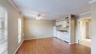 This efficiently designed 1-bedroom, 1-bathroom unit is laid out entirely on a single floor, offering a practical and comfortable living arrangement. The combined kitchen and living area forms the heart of the space, finished with warm hardwood-style flooring and crowned with crown molding and a textured ceiling. A ceiling fan provides year-round comfort, while multiple windows with horizontal blinds allow natural light to flow throughout. The kitchen is positioned along one wall and features white cabinetry, a full-size refrigerator, an electric range, a built-in microwave, and a sink with ample counter space — all finished in a clean, cohesive white palette. The bedroom offers plush carpeted flooring, a ceiling fan, and two large windows that bring in natural light and views of the outdoors. A dedicated closet with wire shelving and a hanging rod provides practical storage. An additional area with hardwood-style flooring and crown molding serves as a versatile entry or secondary living space, also benefiting from natural light. The full bathroom is equipped with a soaking tub and shower combo featuring clean white surrounds and chrome fixtures, completing this well-appointed unit.