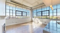 Located at 1360 Niagara St in Buffalo, NY, this 2-bedroom, 3-bathroom unit showcases a striking blend of industrial character and modern refinement. The open-concept living, dining, and kitchen area is the heart of the space, anchored by dramatic floor-to-ceiling factory-style windows with black steel frames that flood the interior with natural light and frame panoramic views of the surrounding waterway and cityscape. Exposed silver ductwork and track lighting along the white-painted ceiling add to the loft-inspired aesthetic, while warm hardwood flooring flows throughout. The kitchen is appointed with crisp white shaker cabinetry, stone countertops, stainless steel appliances including a full refrigerator, range, microwave, and dishwasher, complemented by a classic subway tile backsplash and a generous double-basin island sink. Both bedrooms are well-proportioned with double-door closets and abundant natural light, while the primary bedroom offers a notably spacious footprint. The three bathrooms are clean and contemporary, featuring tile flooring, built-in shelving, and a mix of walk-in glass shower and tub/shower combinations. Additional conveniences include a dedicated laundry room, pantry, and four closets throughout.