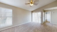 This single-story residence offers a practical and comfortable layout with a clean, neutral aesthetic throughout. The entry foyer welcomes visitors with vaulted ceilings that lend an open, airy feel, transitioning seamlessly into the main living area. The living room is generously proportioned, featuring plush wall-to-wall carpeting, a ceiling fan with integrated lighting, and sliding glass doors dressed with vertical blinds that invite natural light and provide access to the outdoors.

The kitchen is efficiently designed in a galley configuration, showcasing crisp white cabinetry, granite-style countertops, a tile backsplash, and durable wood-look vinyl flooring. Black appliances, including a refrigerator, range, and dishwasher, provide a striking contrast against the bright cabinetry, creating a functional and visually balanced cooking space.

The bedrooms are well-sized, each finished with soft carpeting and windows fitted with horizontal blinds that allow for natural light and privacy. The primary bedroom benefits from a dedicated walk-in closet complete with built-in shelving and hanging rods, offering excellent storage capacity. Throughout the residence, neutral wall tones and consistent flooring choices create a cohesive and inviting atmosphere suited to a variety of interior styles.