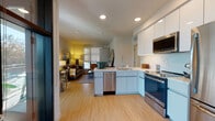 Located at 1626 Lincoln Blvd in Santa Monica, CA, this thoughtfully designed single-floor residence offers a seamless blend of modern style and functional living. The open-concept layout connects the kitchen and living area, creating an inviting and cohesive space. The kitchen is outfitted with sleek white cabinetry, marble-style quartz countertops, stainless steel appliances including a range, built-in microwave, dishwasher, and refrigerator, and a convenient in-unit stacked washer and dryer. Light bamboo-style hardwood flooring runs throughout, adding warmth and continuity. The living area is bathed in natural light through large windows fitted with roller shades, and features a comfortable seating arrangement anchored by a woven area rug. A warm-toned wooden credenza topped with a large round gold-framed mirror adds character to the space. The bedroom provides a peaceful retreat with ample natural light and generous layout. The bathroom is finished with marble-patterned tile flooring, a full soaking tub with shower, and clean white surfaces that create a bright, spa-like atmosphere. Recessed lighting throughout enhances the modern aesthetic of this well-appointed Santa Monica residence.
