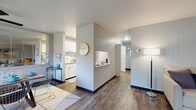 This single-floor residence offers a thoughtfully designed open-concept layout that connects its key living spaces with ease and flow. The galley-style kitchen is a functional highlight, featuring crisp white cabinetry with brushed nickel hardware, light countertops, stainless steel appliances including a refrigerator and dishwasher, and durable wood-look flooring that extends throughout the main areas. A pass-through counter connects the kitchen to the adjacent living spaces, enhancing the open feel.

The living room is generously sized, bathed in natural light from a large window, and finished with the same wood-look flooring. It flows naturally into a dedicated dining area, which features a ceiling fan, additional window views of the outdoors, and a mirrored wall accent that adds depth and brightness to the space.

The unit includes two bedrooms, each finished with plush carpet flooring and neutral gray walls. The primary bedroom is a comfortable retreat with ample space, while the second bedroom benefits from a window with a green outdoor view. The bathroom features a full soaking tub and shower combination with stainless steel grab bars and wood-look flooring. Throughout, the cool gray palette and clean architectural lines create a modern, cohesive ambiance.