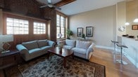 Located at 300 Canal in Lawrence, Massachusetts, this single-floor residence is a beautifully converted historic mill unit that masterfully blends industrial character with modern comfort. The living room is a standout space, showcasing soaring ceilings with exposed wooden beams, original brick accent walls, and oversized multi-pane windows that flood the room with natural light and offer views of the surrounding canal area. Light hardwood flooring runs throughout, complementing the warm, inviting ambiance.

The kitchen is well-appointed with rich honey-toned cabinetry, granite countertops, and a full suite of stainless steel appliances including a refrigerator, range, and built-in microwave. A breakfast bar with a frosted glass partition provides additional seating and separates the kitchen from the living area.

The unit features two bedrooms, each with hardwood floors and exposed beam detailing. One bedroom benefits from a large brick-framed window with outdoor views, while the other includes a spacious closet with built-in shelving. The bathroom is finished with tile flooring, a granite vanity, and a tub-shower combination. A stacked washer and dryer unit is conveniently located within the bathroom, providing practical in-unit laundry. This space offers a compelling combination of historic architectural detail and contemporary finishes.
