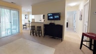 Located at 3001 Reflections Way in Virginia Beach, Virginia, this single-floor residence offers a thoughtfully designed layout that balances comfort and functionality. The open-concept living area serves as the heart of the home, featuring a tiled fireplace, plush carpeting, and sliding glass doors that invite natural light while providing access to a private outdoor patio. A pass-through window connects the living space to a galley-style kitchen, which is outfitted with rich dark wood cabinetry, light granite countertops, wood-look flooring, and black appliances — creating a practical yet stylish workspace. A dedicated dining area sits just beyond, completing the communal zone. The primary bedroom is a serene retreat, featuring carpet flooring, dual nightstands, and generous window coverage that allows soft, diffused light to fill the room. A second bedroom offers additional versatility, highlighted by a built-in window seat with views of greenery and a spacious reach-in closet — ideal as a guest room or home office. The bathroom includes a full tub-and-shower combination with classic tile surround. A dedicated laundry area houses a full-size Whirlpool washer and dryer with overhead wire shelving for added storage. Throughout the residence, neutral tones and consistent finishes create a cohesive and inviting atmosphere.