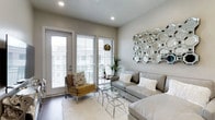 This thoughtfully designed single-floor residence blends contemporary style with functional living. The open-concept kitchen is a standout feature, showcasing striking wood-grain cabinetry that extends floor to ceiling, pristine white quartz countertops, stainless steel appliances including a gas range, and a breakfast bar with pendant lighting and a skylight overhead — creating a bright, welcoming space for cooking and casual dining.

The living area exudes a modern, refined aesthetic, with recessed lighting, wood-look flooring, and large sliding glass doors and a full-light entry door that open to a private balcony, flooding the room with natural light. A large geometric mirrored wall accent serves as a focal point, complementing the neutral color palette throughout.

The primary bedroom offers a serene retreat, featuring warm hardwood flooring, a barn-style sliding door, and soft, diffused natural light through window blinds. A second bedroom provides a cozy atmosphere with wall-mounted TV, plush furnishings, and ample natural light.

The bathroom is finished with dark espresso cabinetry, a vessel sink, a large framed mirror, and light tile flooring, combining practicality with clean, modern design. Throughout the space, consistent neutral tones, quality finishes, and abundant natural light create a cohesive and inviting ambiance.