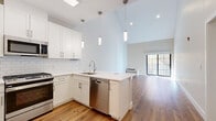 Located at 305 Patterson St in Hillsdale, NJ, this two-story home offers a thoughtfully designed layout spread across two floors. The main level features an open-concept kitchen and living area distinguished by dramatic vaulted ceilings that create an expansive, airy atmosphere. The kitchen is outfitted with white shaker cabinetry, a classic subway tile backsplash, a peninsula with a white quartz countertop, and a full suite of stainless steel appliances including a gas range, built-in microwave, dishwasher, and French door refrigerator. A skylight overhead floods the space with natural light, complementing the warm-toned hardwood flooring that runs throughout the home. The living room opens to a large sliding glass door, bringing in additional natural light and outdoor views of surrounding greenery. The generously sized primary bedroom on the upper level features sloped architectural ceilings, a wall-mounted mini-split HVAC unit, and access to two well-appointed walk-in closets with custom built-in shelving and hanging systems. Both bathrooms are finished in a clean, contemporary style, with one featuring light porcelain tile flooring, a white floating vanity, and a glass-enclosed subway tile shower. The home also includes a dedicated utility room, hallway, and staircase connecting the two floors.