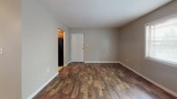 Located at 2702 Industrial Dr in Bowling Green, Kentucky, this single-floor unit offers a well-organized layout with a cohesive, neutral color palette throughout. The living area makes a strong first impression with rich, dark hardwood-style flooring, neutral gray walls, and clean white trim and baseboards. Natural light filters in through a window fitted with horizontal blinds, creating a bright and welcoming atmosphere. The kitchen is a functional highlight, featuring warm-toned wood cabinetry with raised-panel detailing, granite-style countertops, a stainless steel sink, and black appliances including a gas range and refrigerator, all set atop tile flooring. The bedrooms are carpeted in a neutral tone and benefit from generous natural light through multiple windows with blinds, offering a quiet and comfortable feel. The bathroom presents a clean, practical design with a white vanity, integrated sink, overhead lighting, and tile flooring, with a hallway connecting it smoothly to the rest of the unit. Throughout the space, consistent finishes and a straightforward floor plan make for an easy-to-navigate, move-in-ready unit well-suited for everyday living.