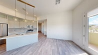 This contemporary single-floor unit offers five bedrooms and two bathrooms across a well-designed, efficiently organized layout. Light wood-style flooring flows consistently throughout the space, complementing the clean white walls and creating a bright, cohesive aesthetic.

The open-concept kitchen and living area serves as the heart of the unit. The kitchen is outfitted with stainless steel appliances — including a French door refrigerator, gas range, and built-in microwave — white shaker-style cabinetry with glass-front upper cabinets, a white quartz countertop island with an undermount sink, and stylish pendant lighting with gold-toned accents. The adjacent living area benefits from large windows and a glass door that invite generous natural light and provide outdoor views.

A central hallway connects the bedrooms, each offering clean, neutral spaces with consistent flooring. The primary bedroom is a comfortable size and is served by a well-appointed en-suite bathroom featuring a dual-sink vanity with quartz countertops, a large framed mirror, and a separate soaking tub and shower combination. The second bathroom includes a glass-enclosed walk-in shower with a built-in bench and subway tile surround. Throughout the unit, the design aesthetic is modern and understated, prioritizing clean lines and functional living.