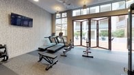 The Town29 Fitness Center is a thoughtfully designed, single-floor facility that offers residents a comprehensive workout experience. The space features durable, multi-toned rubber flooring throughout, providing both safety and comfort during exercise. Large floor-to-ceiling windows flood the interior with abundant natural light, while folding glass doors open directly onto an outdoor courtyard, creating a seamless indoor-outdoor connection and excellent ventilation.

The cardio zone is well-appointed with multiple elliptical trainers, treadmills, a stair climber, and a rowing machine, catering to a wide range of aerobic workouts. A dedicated strength training area houses a multi-functional cable machine for resistance training, complemented by a full rack of dumbbells and a weight bench for free weight exercises. A wall-mounted flat-screen TV enhances the workout experience in the free weights area.

Overhead pendant and track lighting, along with ceiling fans, ensure the space remains comfortable and well-lit at all times. The facility's interior walls feature a textured wallcovering that adds visual warmth, while the bold Town29 skyline mural serves as a standout decorative focal point, reinforcing the community's brand identity throughout the space.