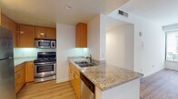 This single-floor residence offers a well-designed layout with modern finishes throughout. The living area is a standout feature, highlighted by a dramatic curved bay window that wraps around a corner, flooding the space with natural light and framing views of the surrounding neighborhood. Light hardwood flooring runs consistently throughout the unit, creating a cohesive and warm aesthetic.

The kitchen is efficiently arranged in a galley-style configuration, outfitted with warm-toned wood cabinetry, granite countertops, and a full suite of stainless steel appliances including a double oven/range, built-in microwave, refrigerator, and dishwasher. A peninsula with a double stainless steel sink and breakfast bar overhang connects the kitchen to the main living area, enhancing the open feel.

A secondary room features its own dedicated window with views of the streetscape, offering a comfortable and naturally lit space. Both bathrooms are finished with granite-topped white vanities, large mirrors, and full tub-shower combinations, maintaining the clean, contemporary style found throughout the unit. Recessed lighting and ample closet storage with double doors contribute to the functional and polished overall ambiance.