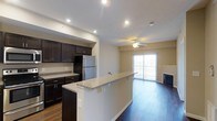 This 1-bedroom, 1-bathroom residence is thoughtfully designed on a single floor, offering an efficient and comfortable open-concept layout. The kitchen is a standout feature, showcasing rich dark cabinetry, granite countertops, and stainless steel appliances, including a full-size refrigerator. A peninsula with a granite overhang extends into the living area, creating a natural bar-height seating space and a seamless transition between cooking and entertaining zones. The flooring throughout is a warm hardwood, adding a cohesive and polished feel to the space. The living area is bright and inviting, equipped with a ceiling fan and recessed lighting that complement the natural light streaming in through a sliding glass door. The sliding door opens to a private balcony, ideal for enjoying outdoor views. A fireplace anchors one wall of the living area, adding a cozy and functional focal point. Recessed lighting throughout the kitchen and living space ensures well-distributed illumination. The overall ambiance is modern and clean, with a neutral color palette that provides a versatile backdrop for a variety of interior styles.