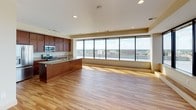 This generously sized two-bedroom, two-bathroom residence offers an open-concept floor plan with warm hardwood flooring throughout the living areas and bedrooms. The kitchen is a standout feature, showcasing rich cherry wood cabinetry extending to the ceiling, granite countertops, stainless steel appliances including a built-in microwave, electric range, and French door refrigerator, and a large center island with an undermount sink — ideal for both everyday living and entertaining.

The expansive living area is framed by a wall of floor-to-ceiling windows that flood the space with natural light and offer impressive panoramic views of the city skyline and waterfront. Both bedrooms continue the hardwood flooring and feature large windows with the same sweeping views. The primary bedroom includes dual closets for generous storage.

The bathrooms are finished with large-format tile flooring, rich wood vanities topped with granite, and glass shower enclosures, maintaining a consistent level of quality throughout. A wide hallway connects the bedrooms and bathrooms, enhancing the sense of flow and spaciousness. Recessed lighting and track lighting add to the bright, modern ambiance of this well-appointed upper-floor residence.