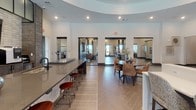 Located in Murfreesboro, Tennessee, this single-floor clubhouse is a thoughtfully designed communal space that blends contemporary style with warm, inviting elements. The open-concept layout is anchored by a dramatic tray ceiling with elegant curved cutouts, accented by recessed lighting and a statement chandelier that together create an airy, sophisticated atmosphere.

The lounge area serves as a central gathering point, highlighted by a floor-to-ceiling stacked stone fireplace wall with a mounted flat-screen television and built-in shelving. Rich hardwood-style flooring, plush leather seating, and curated artwork contribute to the space's refined, residential feel.

Adjacent to the lounge, a dedicated bar and café area features a long countertop with bar stools, beverage dispensers, and a mounted television — ideal for social gatherings. A large round dining table with upholstered chairs provides a comfortable seating option nearby, set atop herringbone-patterned tile flooring that adds visual interest and texture.

Large doorways and open passageways connect the various zones of the space, promoting an easy flow throughout. Abundant natural light filters in through multiple windows and glass doors, enhancing the bright, welcoming ambiance. The overall design balances modern architecture with warm, earthy tones to create a versatile and inviting communal environment.