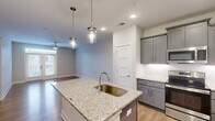 Located at 7100 Summerside Dr in Whitsett, NC, this well-appointed 3-bedroom, 2-bathroom single-story home offers a thoughtfully designed floor plan with modern finishes throughout. The open-concept kitchen and living area serves as the heart of the home, anchored by a central island with granite countertops, an undermount sink, and stylish pendant lighting. Gray shaker-style cabinetry, white subway tile backsplash, stainless steel appliances—including a French door refrigerator and dishwasher—and light wood-style flooring complete the kitchen's contemporary aesthetic. The living room flows seamlessly from the kitchen, featuring a ceiling fan and access to a private balcony through glass-paneled French doors with transom windows that invite abundant natural light. The three bedrooms are carpeted for comfort, each equipped with ceiling fans and windows with neighborhood views. The generously sized primary bedroom offers a spacious feel with ample room for furnishings. The bathrooms echo the home's design language with granite-topped gray vanities, wood-look flooring, and natural light from windows. A dedicated hallway and closet provide practical storage solutions, rounding out this clean, move-in-ready home.