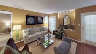 This single-story residence presents a cohesive design scheme anchored by warm golden-tan walls and a mix of hardwood-style and carpeted flooring throughout. The living room is generously proportioned, offering multiple seating areas, track lighting, and several windows with horizontal blinds that allow ample natural light. The space flows naturally into a dedicated dining area, which features pendant lighting and a pass-through window connecting to the kitchen.

The kitchen is well-equipped with white cabinetry, granite-style countertops, black appliances including a coil-top range and over-the-range microwave, a double stainless steel sink, and durable hardwood-style flooring.

The residence includes multiple bedrooms, each finished with plush carpeting, ceiling fans, and windows fitted with blinds. One bedroom features a walk-in closet, while another includes a dedicated workspace area. The warm wall tones carry consistently through each room.

The bathrooms offer tub and shower combinations with white tile surrounds, granite-style vanity countertops, white cabinetry, and hardwood-style flooring, providing a clean, functional finish throughout.