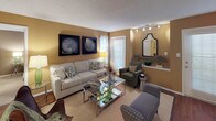 This single-story residence presents a cohesive design scheme anchored by warm golden-tan walls and a mix of hardwood-style and carpeted flooring throughout. The living room is generously proportioned, offering multiple seating areas, track lighting, and several windows with horizontal blinds that allow ample natural light. The space flows naturally into a dedicated dining area, which features pendant lighting and a pass-through window connecting to the kitchen.

The kitchen is well-equipped with white cabinetry, granite-style countertops, black appliances including a coil-top range and over-the-range microwave, a double stainless steel sink, and durable hardwood-style flooring.

The residence includes multiple bedrooms, each finished with plush carpeting, ceiling fans, and windows fitted with blinds. One bedroom features a walk-in closet, while another includes a dedicated workspace area. The warm wall tones carry consistently through each room.

The bathrooms offer tub and shower combinations with white tile surrounds, granite-style vanity countertops, white cabinetry, and hardwood-style flooring, providing a clean, functional finish throughout.