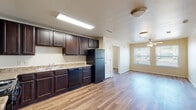 This single-floor unit offers a practical and cohesive layout highlighted by warm wood-look flooring that runs throughout the entire space. The kitchen serves as a functional centerpiece, featuring rich dark espresso cabinetry extending from floor to ceiling, light granite-style countertops, and a full suite of black appliances including a gas range, dishwasher, and refrigerator. A recessed fluorescent light fixture provides bright, even illumination over the workspace, and an under-cabinet range hood adds to the kitchen's utility.

The open layout connects the kitchen seamlessly to a living and dining area, where a ceiling fan with a light kit keeps the space comfortable. Natural light enters through a window fitted with horizontal blinds, offering views of the surrounding area.

The bedrooms are well-proportioned, each featuring the same consistent wood-look flooring, ceiling fans, and windows that bring in natural light. One bedroom includes a double-door closet, providing generous storage space.

The bathroom is finished with matching dark cabinetry, a granite-style vanity countertop, a large mirror with overhead lighting, and a full tub-shower combination set against clean white surrounds. White paneled interior doors with brushed nickel hardware carry a uniform aesthetic throughout the unit, contributing to the space's clean and cohesive overall presentation.