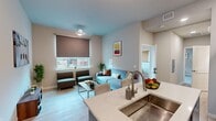 Located at 1332 W Jefferson Blvd in Los Angeles, CA, this 2-bedroom, 1-bathroom unit offers a thoughtfully designed single-floor layout. The open-concept kitchen and living area serves as the heart of the home, featuring light wood-style flooring, a bold blue kitchen island with a stainless steel sink and white quartz countertop, warm wood cabinetry, and a stainless steel refrigerator. The living area accommodates a comfortable seating arrangement with a light blue sofa, armchairs, and a large window fitted with a roller shade that allows natural light to filter in. The primary bedroom is generously sized, with plush carpet flooring, a large window offering outdoor views, and ample space for a bed and study desk. The second bedroom features carpet flooring as well and includes a bunk bed setup, making it a versatile space. Both bedrooms maintain a clean, neutral aesthetic. The bathroom is finished with a patterned tile floor, a tub-shower combination with a decorative curtain, a vanity with an undermount sink, and clean white tile walls. Two hallways connect the spaces efficiently. The unit's overall design is modern and functional, with a consistent neutral color palette accented by contemporary furnishings and decor.