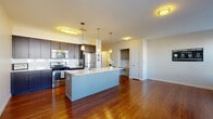This single-floor residence on Upland Woods Circle in Norwood, MA offers a thoughtfully designed open-concept layout with a seamless flow between the kitchen, dining, and living areas. Rich hardwood flooring runs throughout the main living spaces, adding warmth and visual continuity.

The kitchen is a standout feature, equipped with dark espresso cabinetry extending to the ceiling for generous storage, white quartz countertops, a subway tile backsplash, and a full suite of stainless steel appliances including a gas range, microwave, and refrigerator. A large center island with a clean white finish provides additional counter space and casual seating potential. Pendant lighting above the island and flush-mount ceiling fixtures illuminate the space effectively.

The living room benefits from multiple windows that admit abundant natural light and are fitted with horizontal blinds for privacy. Hardwood floors continue here, enhancing the open feel of the space.

Bedrooms feature plush carpeting, ceiling fans, and access to generous closet space, including a walk-in closet outfitted with wire shelving systems for organized storage. One bedroom includes a sliding glass door allowing natural light to fill the room.

The bathroom is finished with large-format tile flooring, a dark-framed vanity mirror, espresso cabinetry, and a tub-shower combination, maintaining the consistent modern aesthetic found throughout the residence.