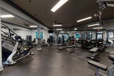 Located at 820 W Marietta St NW in Atlanta, GA, this fitness center is a well-appointed, single-floor facility designed to accommodate a comprehensive workout experience. The space is generously sized, offering ample room for both cardio and strength training activities without feeling crowded.

The layout is anchored by distinctive tiled and stone-accented structural columns that lend a polished, architectural character to the interior. Durable rubber flooring in a speckled dark finish covers the entire space, providing both safety and a sleek, professional aesthetic. The ceiling features recessed linear lighting alongside ceiling fans, ensuring the space remains well-lit and comfortable throughout.

Large, floor-to-ceiling mirrors line multiple walls, enhancing the sense of openness and allowing users to monitor their form during workouts. Expansive windows and glass-panel doors along the perimeter flood the space with natural light and offer views of the surrounding outdoor areas.

The cardio zone is equipped with treadmills, ellipticals, stair climbers, and stationary bikes, all positioned near the windows to take advantage of the natural light. The strength training area includes a full rack of dumbbells, adjustable benches, cable machines, and multi-function weight stations. Accent artwork in blue tones adds a touch of color to the otherwise modern, neutral palette, creating an energizing yet focused atmosphere.