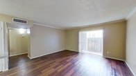 This single-floor residence offers a well-organized layout designed for comfortable everyday living. The spacious living area is highlighted by rich, dark hardwood-style flooring that runs throughout the main living spaces, crown molding along the ceiling perimeter, and a textured ceiling finish. A large sliding glass door floods the room with natural light while providing direct access to the outdoors, complemented by vertical blinds for privacy and light control. The front entryway opens into this generous living space, offering a clean, open feel.

The galley-style kitchen is efficiently designed with ample dark wood cabinetry above and below the countertops on both sides, white appliances including a coil-burner range, oven, and refrigerator, as well as a dishwasher and sink. Hardwood-style flooring continues through the kitchen, and overhead lighting ensures a well-lit workspace.

The bedrooms are carpeted for comfort and each features a ceiling fan with lighting. The rooms are neutrally painted with beige tones, providing a calm and versatile backdrop. The bathroom is equipped with a full-size soaking tub and shower combination, featuring a clean white surround with built-in shelving and brushed nickel fixtures, alongside a toilet and vanity area.