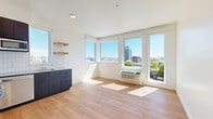 This thoughtfully designed one-bedroom, one-bathroom unit offers a clean, contemporary aesthetic throughout. Light wood-tone flooring flows seamlessly across every room, complementing the crisp white walls and creating a bright, cohesive feel.

The open-concept living and kitchen area is a standout, anchored by a well-appointed kitchen featuring dark navy cabinetry, white subway tile backsplash, stainless steel appliances including a gas range, dishwasher, refrigerator, and built-in microwave, along with open wood floating shelves. A wall of large windows floods the space with abundant natural light and offers impressive elevated views of the surrounding cityscape and distant hills.

The bedroom is a quiet, comfortable retreat with a ceiling fan, a dedicated window framing more urban views, and direct access to a walk-in closet equipped with wire shelving and hanging rods for organized storage.

The bathroom maintains the unit's modern sensibility with light wood-tone flooring, a floating vanity with an undermount sink and quartz countertop, a large mirror, and matte black hardware accents throughout.

A clean, well-lit hallway with recessed lighting connects all rooms efficiently. The unit's layout maximizes every square foot, making it a functional and stylish urban living space.