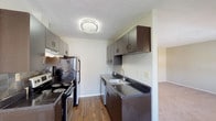 This single-floor residence at 7477 Shady Water Lane in Dayton, Ohio offers a well-organized layout with functional living spaces throughout. The galley-style kitchen is a standout feature, appointed with dark espresso cabinetry, dark countertops, a tiled backsplash, wood-look flooring, a stainless steel range, a refrigerator, and a double-basin sink with a dishwasher. Ample upper and lower cabinet storage lines both sides of the kitchen, maximizing efficiency in the space.

The living area is warm and inviting, anchored by a tile-surround fireplace that serves as a central focal point. Soft carpet flooring extends throughout the living and bedroom areas, contributing to a comfortable atmosphere. The bedrooms are well-proportioned, with large windows that invite natural light — one bedroom features an expansive multi-panel window providing a bright, open feel, while another offers a single window with views of surrounding greenery.

The bathroom is cleanly finished with wood-look flooring, a dark vanity with a single sink, a large mirror, and a tub-shower combination with a white surround. Textured ceilings are consistent throughout the home. The overall layout, as seen in the dollhouse view, flows cohesively from the kitchen through the living space and into the bedroom and bathroom areas.