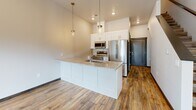 Located at 1021 Blazing Star Blvd in Altoona, Wisconsin, this two-bedroom, two-bathroom home spans two floors with a well-designed layout. The main level features an open-concept kitchen and living area highlighted by rich wood-look plank flooring, recessed lighting, and abundant natural light through sliding glass doors that open to outdoor views of the surrounding greenery. The kitchen is equipped with white shaker cabinetry, stainless steel appliances including a refrigerator, microwave, and range, complemented by a granite-topped center island with pendant lighting above — a standout feature of the main living space. The living room is bright and spacious, with additional sliding door access to the outdoors. Upstairs, the generously sized primary bedroom features plush carpeting, a ceiling fan, and a private en-suite bathroom and walk-in closet with built-in shelving for ample storage. The second bedroom is well-lit with multiple windows and a stylish barn-style door. Bathrooms are finished with granite vanity tops and white cabinetry. A convenient mudroom area with bench seating and coat hooks adds everyday practicality. Dark wood trim and door accents throughout provide a cohesive, modern aesthetic across both levels.