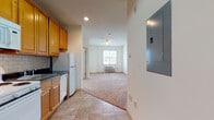 This single-floor unit offers a practical and comfortable layout that flows seamlessly from the kitchen through to the living area. The kitchen is well-equipped, featuring warm honey-toned cabinetry, dark granite countertops, a classic subway tile backsplash, and white appliances including a range, over-the-range microwave, refrigerator, and dishwasher. Tile flooring runs throughout the kitchen, providing a clean and durable surface. The open-concept living area transitions from tile to plush carpeting, creating a cozy and inviting atmosphere. A ceiling fan overhead and a wall-mounted HVAC unit ensure year-round comfort, while a window allows natural light to brighten the space. The bedroom is a quiet, carpeted retreat with neutral walls and ample room for furnishings. The bathroom is clean and functional, featuring tile flooring, a shower-tub combination with a curtain rod, and a toilet. An electrical panel is conveniently accessible near the entryway. Throughout the unit, neutral wall tones and consistent finishes create a cohesive and move-in-ready environment suited for comfortable everyday living.