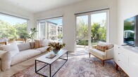 Located at 730 16th Street within The Mansion community in Sacramento, this single-floor residence offers three bedrooms and two bathrooms across a generously sized, thoughtfully designed floor plan. The interior reflects a clean, contemporary aesthetic throughout, with light-toned luxury vinyl plank flooring in the main living areas and plush carpet in the bedrooms.

The open-concept living area is anchored by oversized floor-to-ceiling windows and sliding glass doors that frame lush tree canopy views and flood the space with natural light. The kitchen is well-appointed with two-tone cabinetry—combining sleek gray upper cabinets with warm wood-grain lower cabinets—stainless steel appliances, a white subway tile backsplash, and a large central island with bar seating, making it ideal for both daily living and entertaining.

The bedrooms are bright and serene, featuring neutral finishes and ample space. Both bathrooms are finished with modern wood-tone vanities, white quartz countertops, and clean chrome fixtures; one bathroom includes a tub-shower combination with elegant marble-style tile surround. A dedicated laundry area houses a full-size stacked washer and dryer. The overall ambiance is calm, bright, and modern.