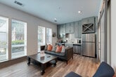 Located at 550 E Brooklyn Village Ave in uptown Charlotte, NC, this thoughtfully designed one-bedroom, one-bathroom residence offers a modern aesthetic with high-quality finishes throughout. The open-concept kitchen and living area serves as the heart of the unit, featuring warm hardwood-style flooring, recessed lighting, and large windows that flood the space with natural light and offer views of the surrounding neighborhood. The kitchen is outfitted with sage-green shaker-style cabinetry, stainless steel appliances including a refrigerator, range, and microwave, a classic white subway tile backsplash, and light quartz countertops. A hallway with sliding barn-style doors connects the living area to the private bedroom, which is a well-proportioned retreat with soaring ceilings, a ceiling fan, and direct access to the bathroom. The bathroom features light-tiled flooring, a white vanity with ample storage, and a clean, neutral palette. Throughout the unit, gray-trimmed doors and sliding hardware provide a cohesive contemporary design element. The combination of modern finishes, an efficient layout, and a prime urban location makes this a standout residence in the heart of Charlotte.
