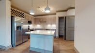 Located on Deer Drive in Lakewood Ranch, Florida, this single-story residence offers a cohesive, contemporary design highlighted by light wood-style flooring, crown molding, and a neutral color palette throughout. The kitchen serves as a central focus of the home, featuring light wood cabinetry, a full suite of stainless steel appliances, subway tile backsplash, under-cabinet lighting, and a freestanding center island topped with a crisp white countertop. Stylish pendant lights hang above the island, adding a modern touch. A decorative wine rack adds character above the refrigerator. Adjacent to the kitchen, a built-in desk area provides a practical workspace. A walk-in pantry offers generous storage. The living areas are carpeted and generously proportioned, with ceiling fans providing comfort. Multiple windows allow natural light to fill the rooms. The primary bedroom is notably spacious, with dual windows, carpet flooring, and access to a walk-in closet. A dedicated laundry area with washer and dryer hookups is conveniently accessible from the bedroom. Two bathrooms are present: one featuring a soaking tub with shower combination and wood-toned vanity, and another with a walk-in shower, large mirror, and multi-drawer vanity, both finished with wood-look flooring.