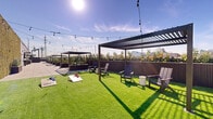 Located at 821 E Main St in Stamford, Connecticut, this rooftop amenity deck offers a thoughtfully designed outdoor retreat with a variety of recreational and social spaces. The expansive rooftop is divided into distinct zones, each catering to a different experience while maintaining a cohesive, modern aesthetic throughout.

A generous artificial turf lawn serves as the centerpiece of the rooftop, lined with Adirondack-style seating and multiple sleek pergolas draped with café string lights that create an inviting ambiance both day and night. Cornhole boards are set up across the lawn, making it an ideal space for casual outdoor recreation and social gatherings.

Adjacent to the turf area, a dedicated children's play zone features a charming playhouse, stepping stones, a Connect Four game, and additional play structures, all set against a living green wall backdrop and open sky views of the surrounding Stamford skyline.

A paved terrace section provides a more structured setting with outdoor dining tables and chairs, surrounded by tall planted greenery in modern wood-paneled planters that add texture and privacy. The planting throughout the rooftop softens the urban environment and enhances the sense of a garden-like escape.

The entire deck enjoys abundant natural sunlight and panoramic views of the Stamford cityscape, making it a versatile amenity space suited for relaxation, entertainment, and community engagement.
