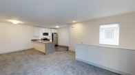 Located at Greenview Village in Islip, New York, this single-floor residence offers a clean, modern aesthetic with an open and functional layout. The kitchen serves as a central highlight of the space, outfitted with crisp white cabinetry, stainless steel appliances including a refrigerator, range, and built-in microwave, and a gray kitchen island with an integrated sink. The island provides both additional counter space and a natural transition point between the kitchen and the adjacent living area. The kitchen features durable wood-look flooring, while the living area is finished with plush carpeting, creating a comfortable and visually distinct zone for relaxing and entertaining. Bright white walls throughout contribute to a light and airy atmosphere, enhanced by flush-mount ceiling lighting. A window in the living area allows natural light to filter into the space. The overall design is neutral and contemporary, making the unit move-in ready and highly versatile. Greenview Village is situated in Islip, New York, a community on Long Island's South Shore known for its residential neighborhoods and convenient access to local amenities.