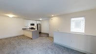 Located at Greenview Village in Islip, New York, this single-floor residence offers a clean, modern aesthetic with an open and functional layout. The kitchen serves as a central highlight of the space, outfitted with crisp white cabinetry, stainless steel appliances including a refrigerator, range, and built-in microwave, and a gray kitchen island with an integrated sink. The island provides both additional counter space and a natural transition point between the kitchen and the adjacent living area. The kitchen features durable wood-look flooring, while the living area is finished with plush carpeting, creating a comfortable and visually distinct zone for relaxing and entertaining. Bright white walls throughout contribute to a light and airy atmosphere, enhanced by flush-mount ceiling lighting. A window in the living area allows natural light to filter into the space. The overall design is neutral and contemporary, making the unit move-in ready and highly versatile. Greenview Village is situated in Islip, New York, a community on Long Island's South Shore known for its residential neighborhoods and convenient access to local amenities.