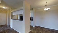 This single-floor residence at 920 Upgrade offers a thoughtfully designed open layout that promotes a seamless flow between living spaces. Dark hardwood-style flooring runs throughout, providing a rich, grounding contrast to the neutral, warm-toned walls and bright white trim work.

A defining architectural feature is the pass-through cutout connecting the kitchen to the adjacent living and dining areas. This opening enhances the sense of openness while maintaining a subtle division between spaces. The kitchen is outfitted with crisp white cabinetry that extends to the upper walls, offering ample storage, and is complemented by a dark stone tile backsplash that adds texture and visual interest. A dark countertop runs along the pass-through bar area, providing a practical surface for casual dining or serving.

Crown molding frames the ceilings in the living and dining areas, adding a refined architectural touch. Ceiling-mounted light fixtures provide consistent illumination throughout. The living and dining spaces are open and well-proportioned, benefiting from the connected layout that allows light and sightlines to travel freely across the floor plan.

Overall, the space presents a clean, updated aesthetic with a cohesive combination of classic white finishes, warm neutral tones, and dark flooring accents that create an inviting and functional home environment.