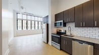 This single-floor urban loft showcases a striking blend of industrial and contemporary design throughout. The open living area commands attention with its soaring ceilings, polished concrete flooring, and an expansive wall of floor-to-ceiling industrial-style windows framed in bold black steel. The oversized windows flood the space with abundant natural light while offering impressive views of the surrounding urban streetscape.

The kitchen is thoughtfully designed and features dark espresso-toned cabinetry with sleek bar-pull hardware, a classic white subway tile backsplash, granite countertops, and a full suite of stainless steel appliances including a refrigerator, electric range, built-in microwave, and dishwasher. Ample upper and lower cabinet storage adds both style and practicality to the space.

Track lighting runs along the ceiling, providing flexible, directed illumination throughout the open-plan living and kitchen areas. The bathroom is clean and modern, with a dark wood vanity, a mirrored medicine cabinet, white countertop, and a combined tub and shower. The consistent use of polished concrete flooring throughout ties the space together, reinforcing the loft's cohesive industrial-modern aesthetic.