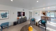 This single-floor clubhouse is thoughtfully designed to serve as a welcoming community hub, blending modern aesthetics with functional amenities. The open-concept layout seamlessly connects several distinct areas, creating a fluid and inviting atmosphere throughout.

The main lounge area features plush seating, including leather accent chairs accented with teal throw pillows, arranged around a central coffee table. A wall-mounted flat-screen television sits atop a dark, vintage-style credenza, making this space ideal for casual gatherings. Recessed lighting and large windows allow natural light to fill the room, complementing the neutral-toned carpet.

Adjacent to the lounge, a dedicated dining area offers a spacious rectangular table surrounded by mid-century modern wood and leather chairs. A striking geometric chandelier with glass globe accents anchors the space above, while large sliding glass doors open to outdoor views, enhancing the sense of openness.

The fully equipped kitchen is a standout feature, showcasing rich wood cabinetry, light quartz countertops, and a dramatic metallic subway tile backsplash. Professional-grade stainless steel appliances — including a gas range with hood, built-in microwave, and refrigerator — make this kitchen well-suited for events and catered functions. A glass door from the kitchen leads directly to an outdoor patio area.

A connected leasing office corridor with herringbone-patterned flooring and glass-panel doors completes this well-rounded clubhouse.