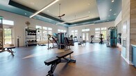 Located at 786 Parker Forest Dr in Dawsonville, Georgia, this fitness center offers a thoughtfully designed, single-floor workout facility that combines functionality with a modern aesthetic. The space is defined by its striking tray ceilings accented in deep teal, recessed lighting, and linear LED fixtures that create a bright, energizing atmosphere. Large ceiling fans help maintain a comfortable environment throughout.

The facility is generously sized, providing ample room to accommodate a comprehensive range of equipment. Cardio offerings include multiple Matrix treadmills and stationary bikes, as well as rowing machines positioned on a distinctive two-tone flooring design. The strength training area features a multi-station cable machine, a variety of weight machines, an adjustable bench, and a well-stocked dumbbell and medicine ball rack for functional training.

Natural light pours in through expansive windows on multiple walls, offering pleasant outdoor views of the surrounding Georgia landscape and greenery. Glass-panel double doors provide direct access to the exterior, further connecting the interior to the outdoors. Accent walls featuring stone and brick detailing add warmth and texture, while large mirrors enhance the sense of space. The overall ambiance is clean, modern, and inviting, making this fitness center a well-rounded amenity for those seeking a comprehensive exercise experience.