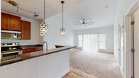 Located at 4200 Academy Dr in Opelika, Alabama, this 2-bedroom, 2-bathroom single-floor residence offers a well-designed layout that maximizes its comfortable footprint. The open-concept kitchen is a standout feature, showcasing rich cherry wood cabinetry, dark granite countertops, stainless steel appliances including a range and microwave, and warm terra cotta tile flooring. A peninsula with a beadboard base and pendant lighting serves as a natural divider between the kitchen and the living area, which transitions to soft carpet underfoot and features soaring vaulted ceilings with a ceiling fan, creating an airy, spacious feel. Large windows and a sliding glass door flood the living space with natural light and offer views of the surrounding greenery. The primary bedroom continues the vaulted ceiling design with an additional ceiling fan, a walk-in closet, and a private en-suite bathroom. The en-suite bath features cherry wood vanity cabinetry, granite countertops, and terra cotta tile flooring with a full tub-shower combination. The second bedroom is bright and carpeted with a large window overlooking outdoor greenery. A dedicated laundry area and a hallway connecting all rooms complete this functional and stylish home.