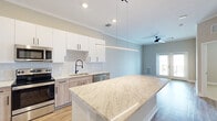 Located at 4090 Rio Vista Dr in Colorado Springs, CO, this thoughtfully designed one-bedroom, one-bathroom residence offers a efficient and modern single-floor layout. The open-concept kitchen and living area serves as the heart of the home, showcasing a large granite-topped island with pendant lighting overhead, white upper cabinetry paired with light wood-toned lower cabinets, a classic subway tile backsplash, and a full suite of stainless steel appliances including a refrigerator, electric range, microwave, and dishwasher. Light wood-look flooring flows throughout the main living areas, complementing the neutral color palette and crown molding details. The living room is bright and airy, featuring a ceiling fan, crown molding, and French doors that invite natural light and provide outdoor access. The bedroom is carpeted and offers a quiet, comfortable retreat with a dedicated closet. The bathroom includes a tub-shower combo with white subway tile surround, wood-look flooring, granite countertops, and white cabinetry with matte black hardware. Recessed lighting and clean architectural lines give this residence a polished, contemporary feel throughout.