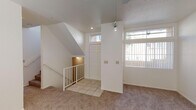 This two-story home is designed with a practical and open layout spread across two levels. The main level begins with a tiled entryway framed by a paneled front door with a transom window above, allowing natural light to filter into the space. Adjacent to the entry, the living area features neutral carpet, a ceiling fan, and a large window that brings in additional daylight. A staircase with white railings connects to the upper level, while a pendant light adds a subtle architectural detail to the open vertical space.

The kitchen is situated on the main floor and includes light-toned cabinetry, a tiled countertop island, wood-look flooring, and white appliances including a range, microwave, and side-by-side refrigerator. A window above the sink provides natural light. A half bathroom on this level features wood-look flooring, a vanity with under-cabinet storage, and a large mirror.

Upstairs, the primary bedroom offers vaulted ceilings, carpet flooring, a ceiling fan, and a window with outdoor views. It connects to a generous walk-in closet with wrap-around rod and shelf storage. The primary bathroom features a dual-sink vanity with ample counter space and wood-look flooring. A secondary full bathroom includes a tub-shower combination with white tile surround and a privacy window.